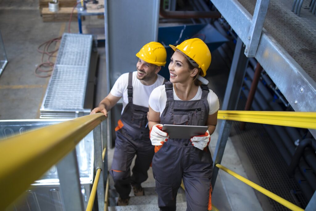 Engineers in protective equipment assessing a site, climbing plant stairs with a tablet