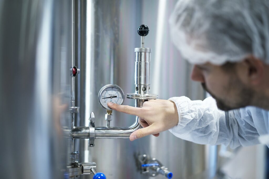 Technician in protective equipment checking a pressure gauge on an industrial utility system