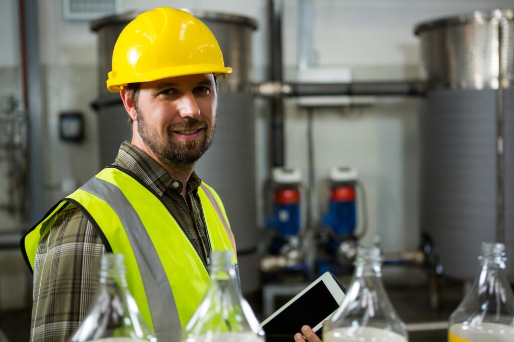 Engineer in protective equipment assessing plant capacity with a tablet beside process tanks
