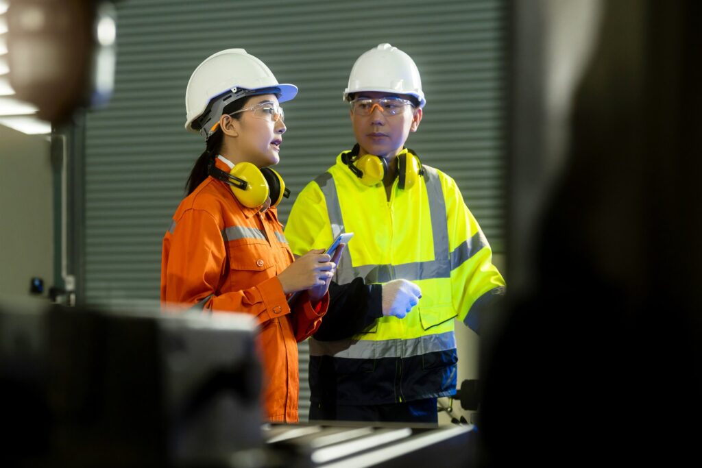 Two engineers in protective equipment inspecting a utility control system with a tablet