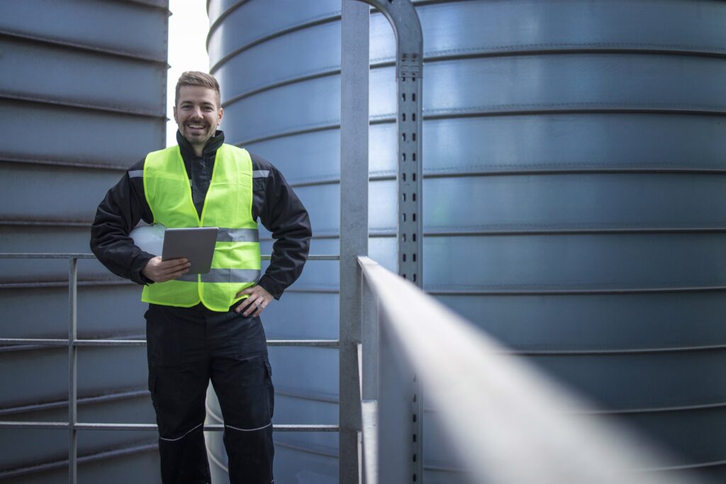 EM3 engineer with a tablet beside industrial storage tanks on a client site
