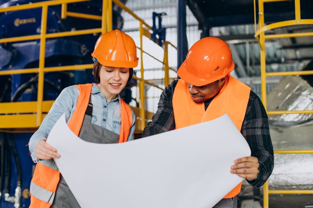 Two workers reviewing a project plan on an industrial plant floor