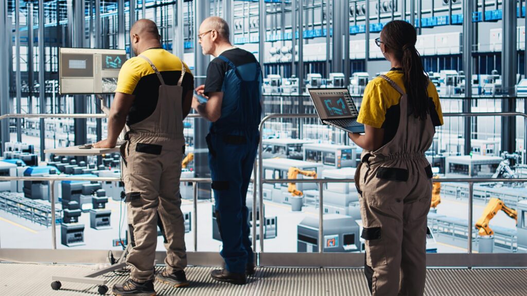 Engineers evaluating an automated industrial plant from a gantry with a laptop