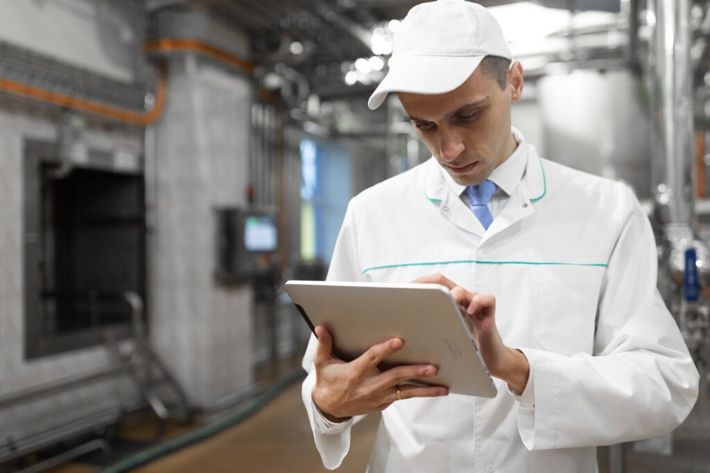 Technologist reviewing energy and process data on a tablet beside plant equipment