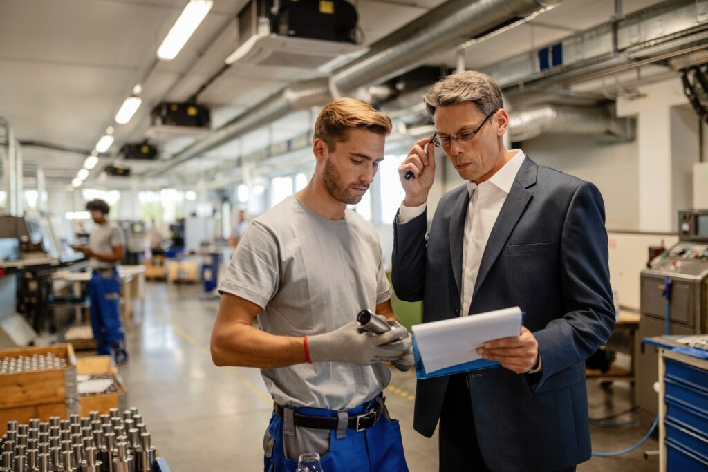 A senior engineer and a worker analysing performance reports together on a factory floor