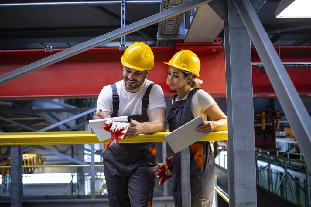 Two engineers in protective equipment reviewing a site assessment on an industrial plant floor