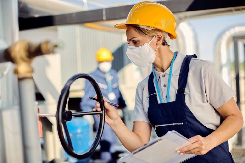Inspector in protective equipment verifying a valve at an industrial facility