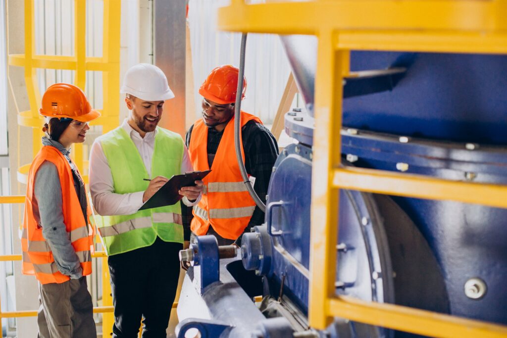 Three engineers in protective equipment reviewing a design plan on a plant floor