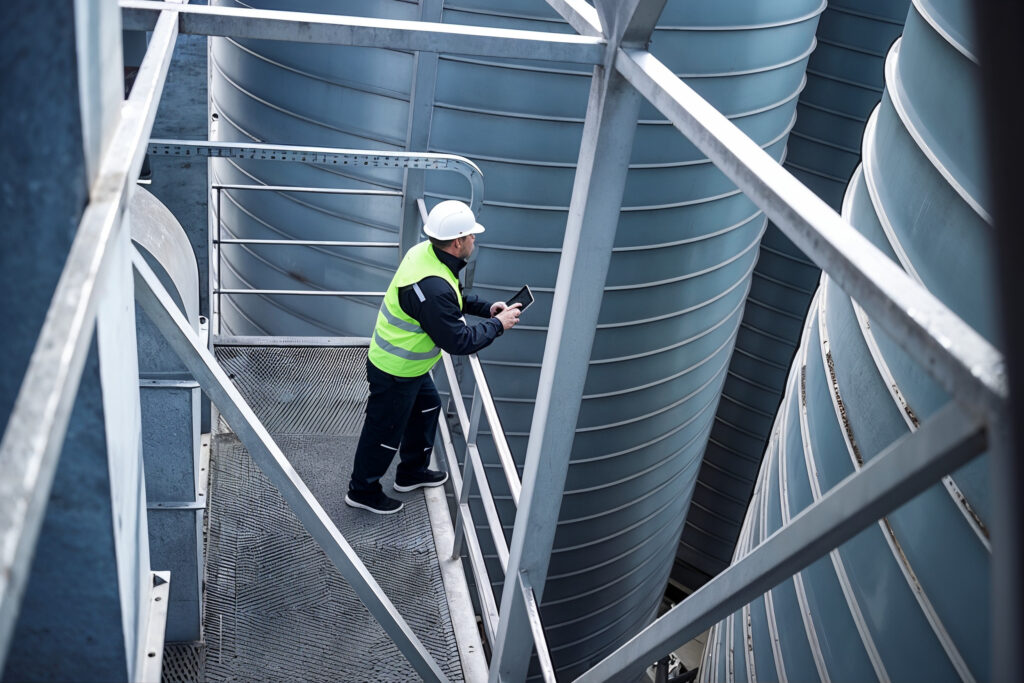 Engineer in hi-vis vest and hard hat reviewing data on a tablet on an industrial plant platform