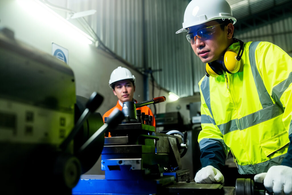 Two maintenance engineers in PPE investigating an industrial machine system on a factory floor