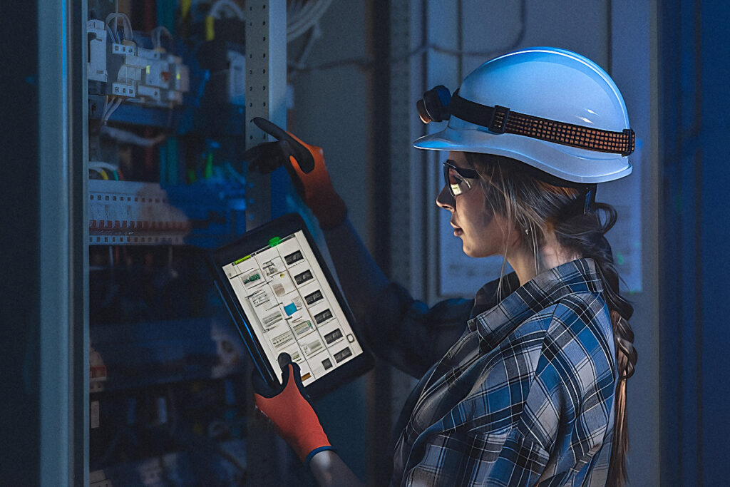 Energy engineer inspecting switchgear and metering on a plant floor in cool blue light
