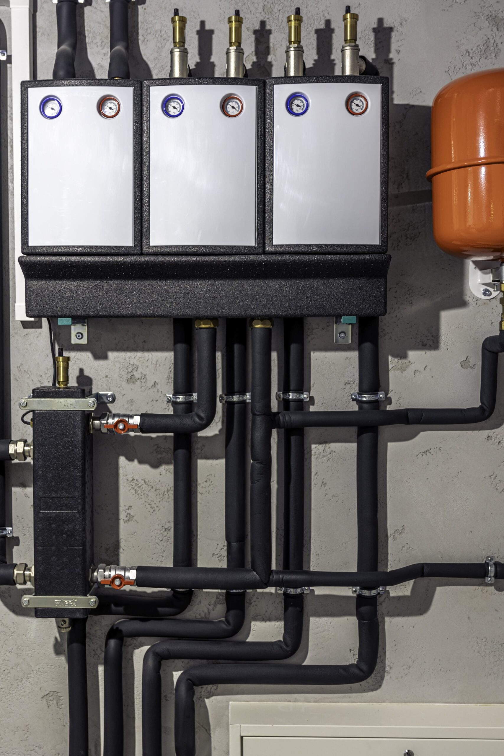 A modern heating plant installation with wall-mounted manifolds, pressure gauges, an expansion vessel and insulated pipework