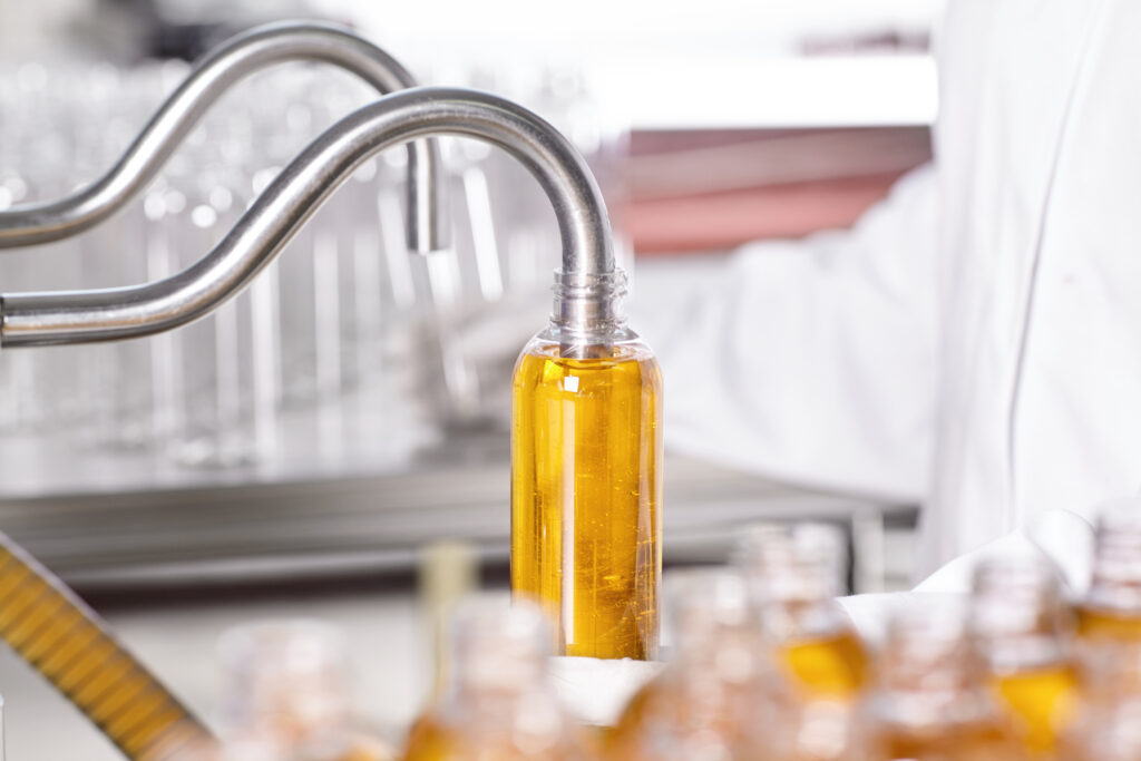 A factory worker in a white gown and gloves inspecting a bottle on a beverage line
