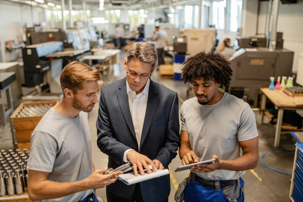 An engineer and two plant operators reviewing quality reports together on a factory floor