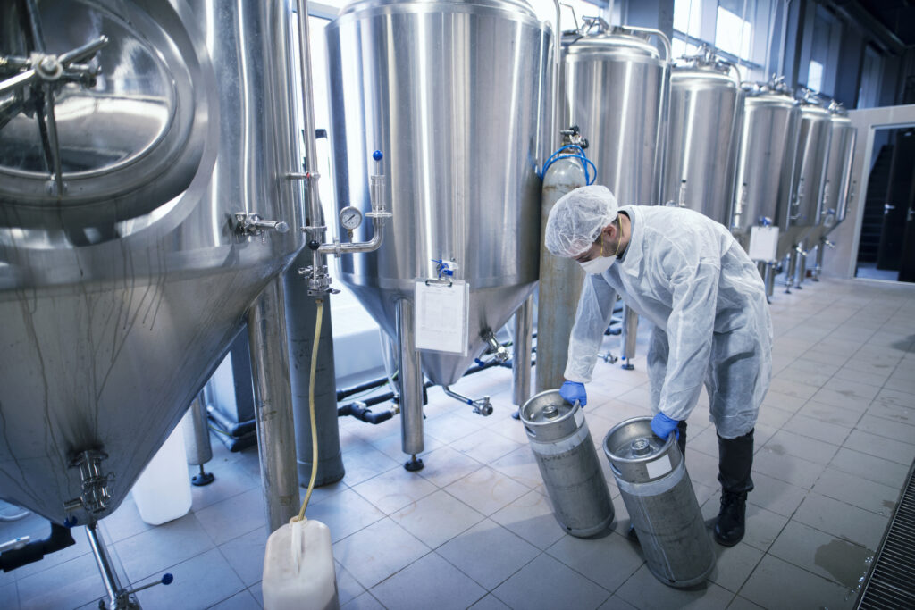 A worker in a protective suit handling chemicals beside metal process reservoirs