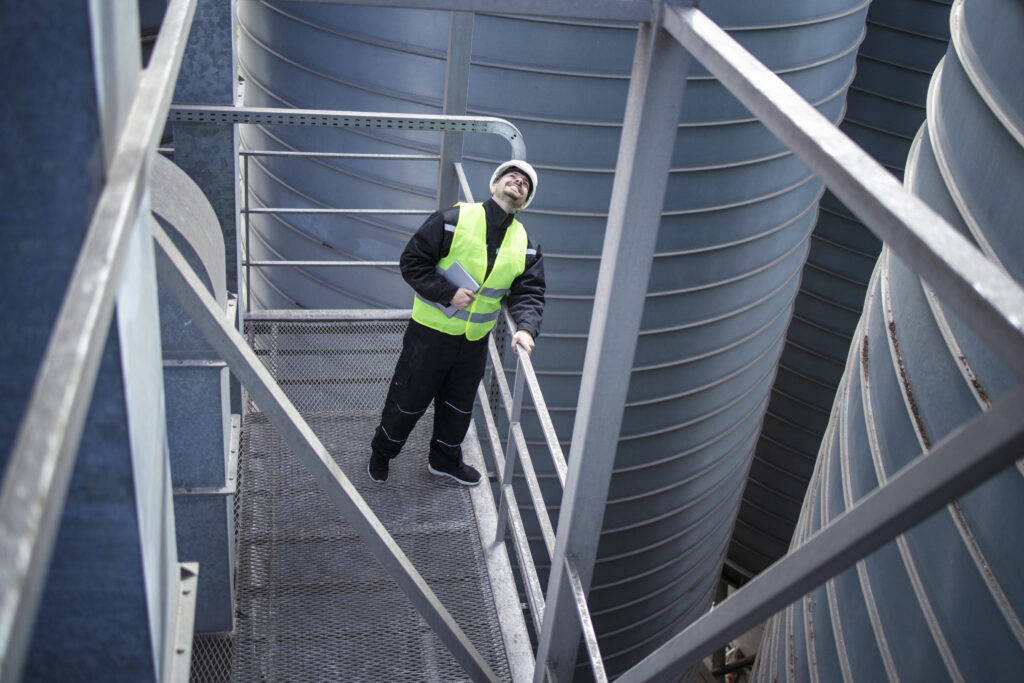 Engineer on a walkway inspecting large industrial storage silos at a food production facility