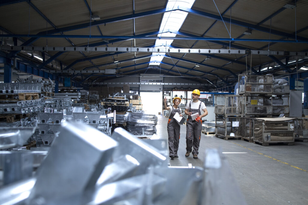 Two workers in hard hats walking through a bright industrial production hall