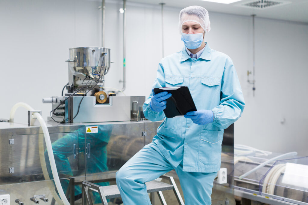 Engineer on a platform inspecting a large stainless steel process vessel in a cleanroom
