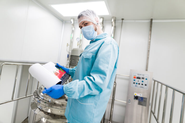 Technician in cleanroom PPE reviewing performance data on a tablet inside a production area
