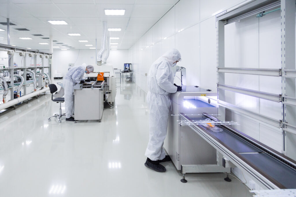 Two operators in white cleanroom suits and gloves working at modern pharmaceutical equipment