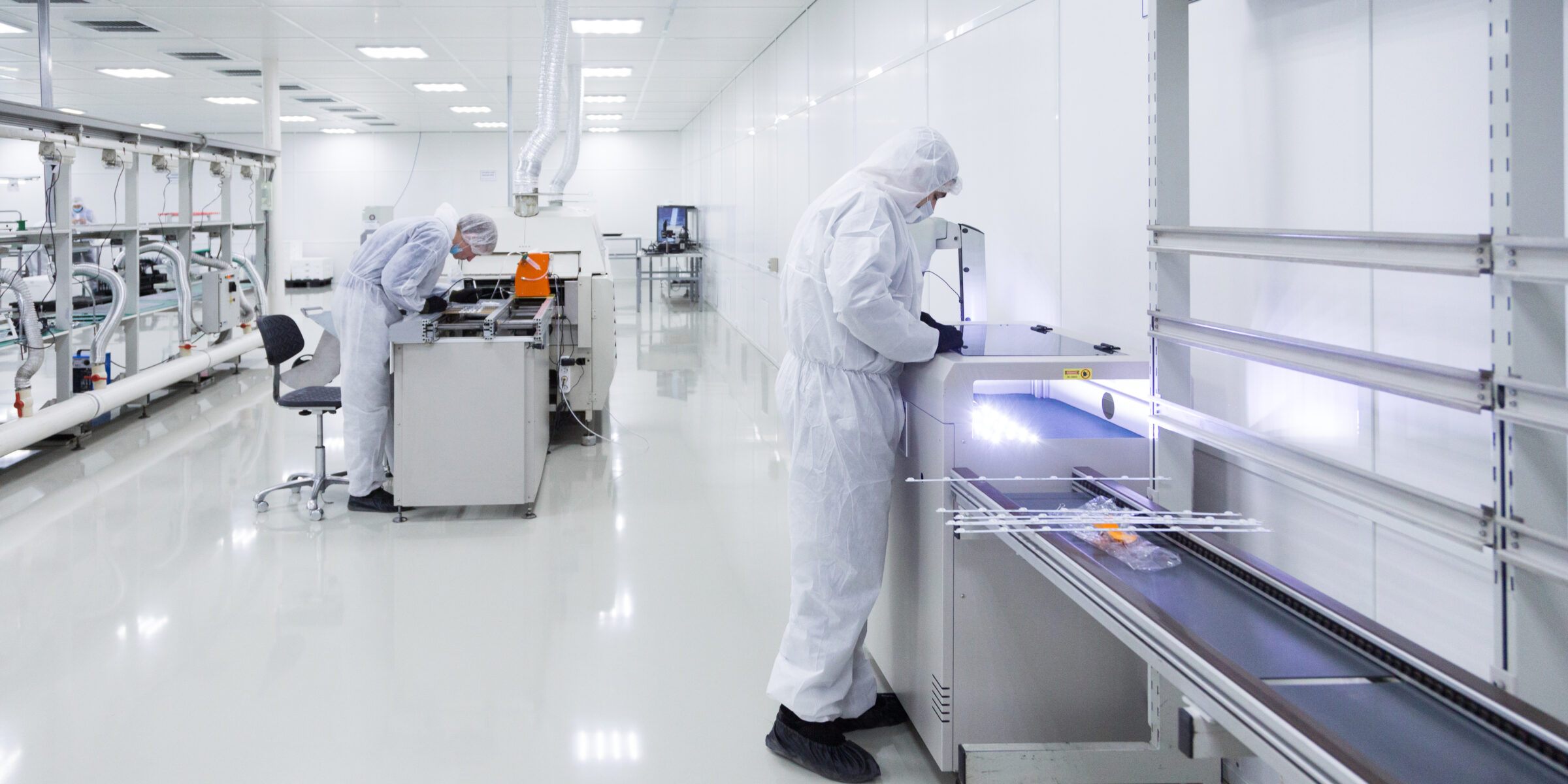 Two operators in white cleanroom suits and gloves working at modern pharmaceutical equipment